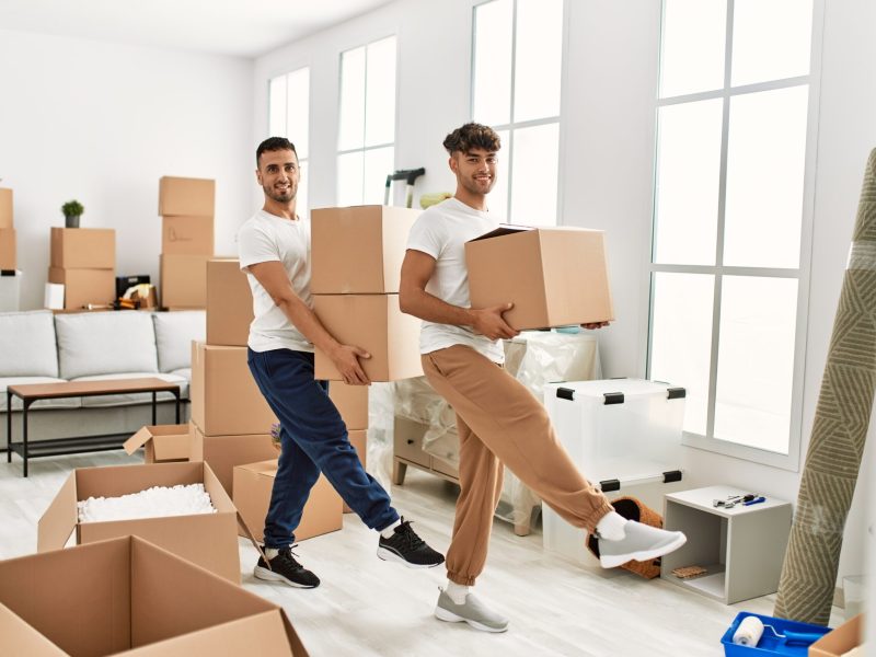 Two hispanic men couple smiling confident holding cardboard boxes at new home